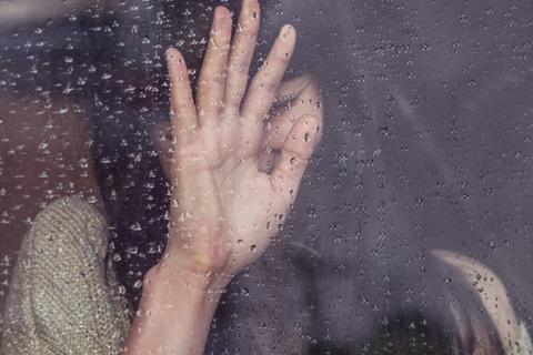 Close-up of a stressed woman through a rainy window.